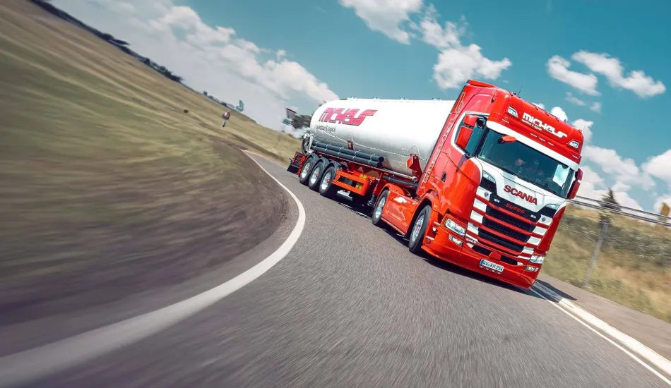 Roter Lkw mit Tankanhänger auf kurviger Straße.